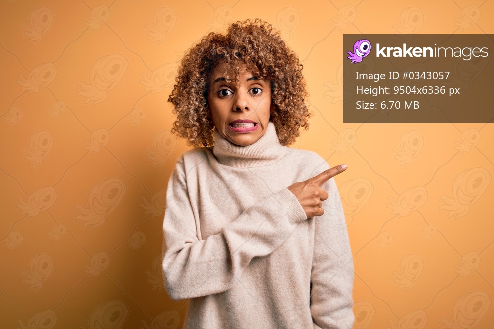 Young beautiful african american woman wearing turtleneck sweater over yellow background Pointing aside worried and nervous with forefinger, concerned and surprised expression