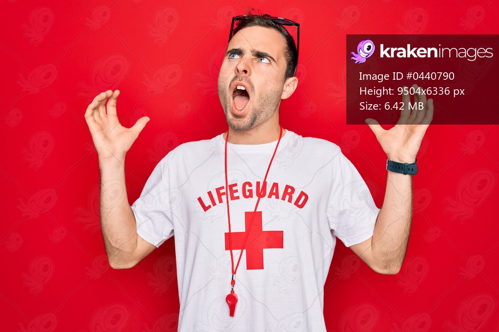 Handsome lifeguard man wearing t-shirt with red cross and whistle over isolated background crazy and mad shouting and yelling with aggressive expression and arms raised. Frustration concept.