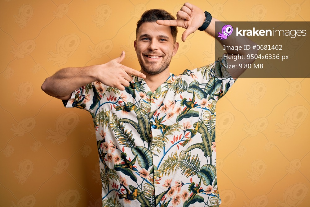 Young man with blue eyes on vacation wearing floral summer shirt over yellow background smiling making frame with hands and fingers with happy face. Creativity and photography concept.