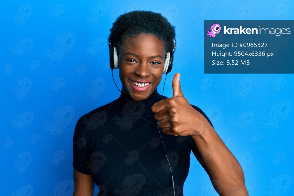 Young african american girl listening to music using headphones smiling happy and positive, thumb up doing excellent and approval sign 