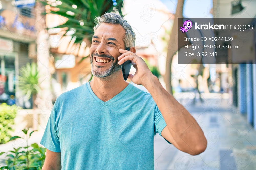Middle age grey-haired man talking on the smartphone walking at street of city.