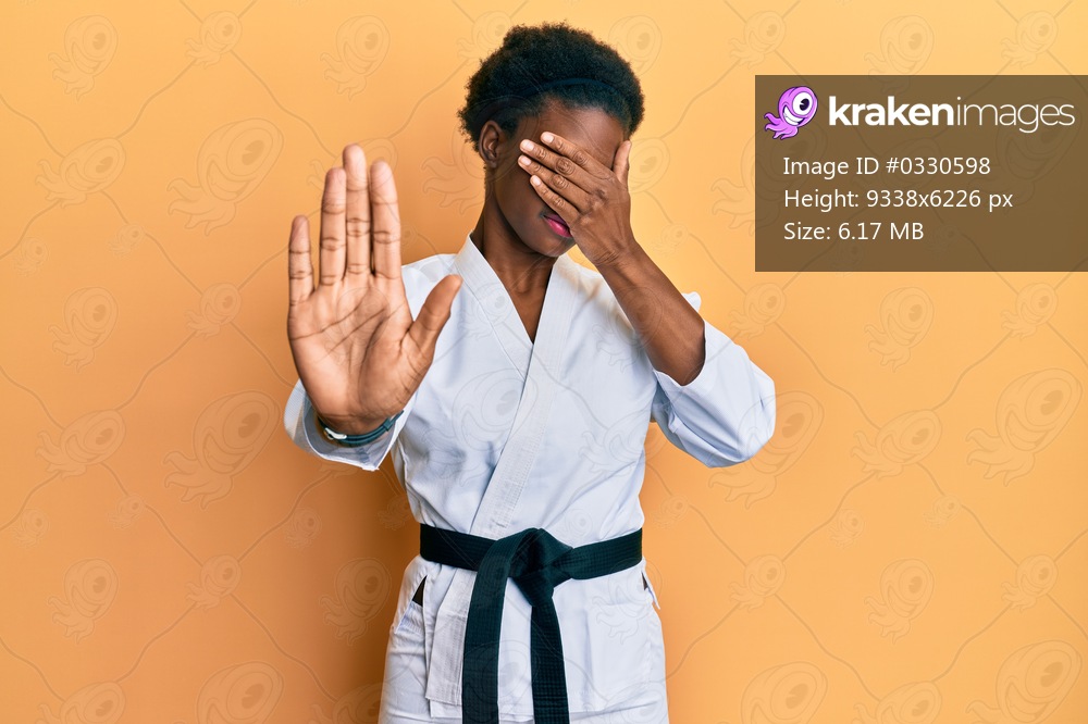Young african american girl wearing karate kimono and black belt covering eyes with hands and doing stop gesture with sad and fear expression. embarrassed and negative concept. 