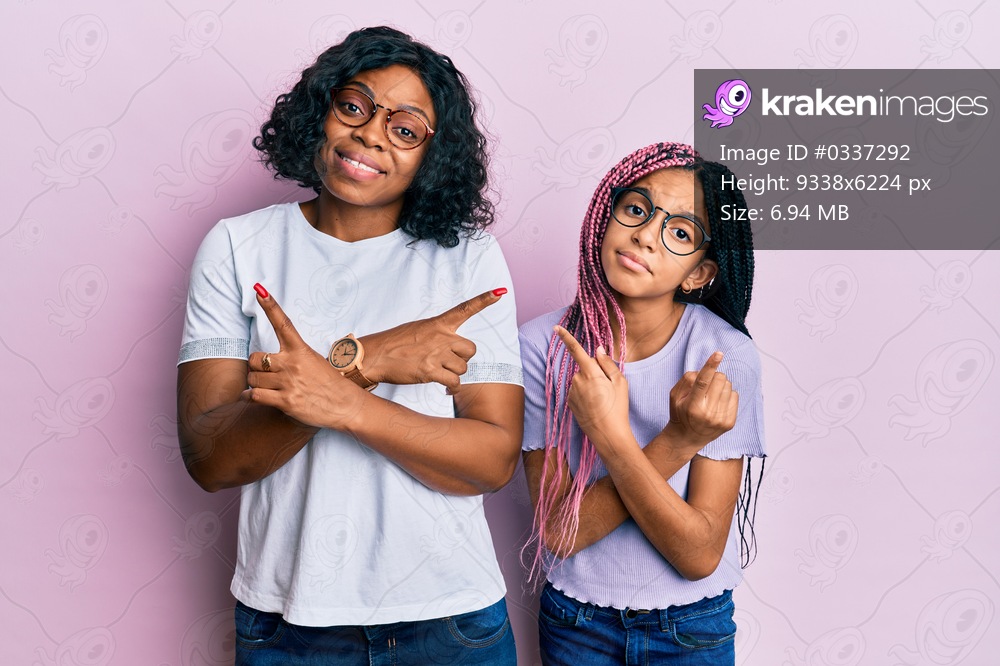 Beautiful african american mother and daughter wearing casual clothes and glasses pointing to both sides with fingers, different direction disagree 