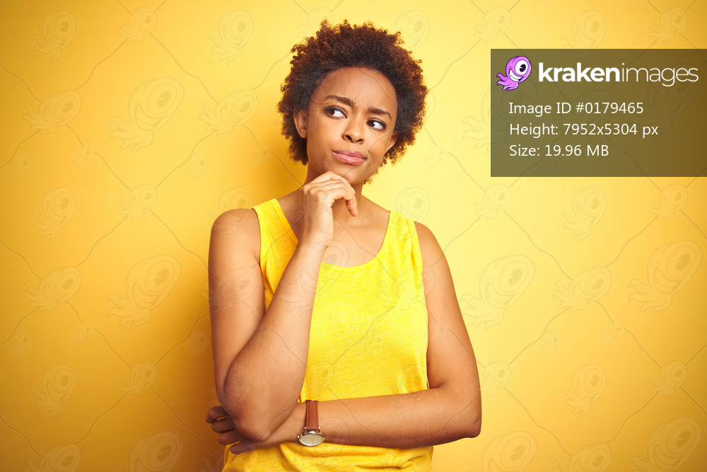 Beauitul african american woman wearing summer t-shirt over isolated yellow background with hand on chin thinking about question, pensive expression. Smiling with thoughtful face. Doubt concept.