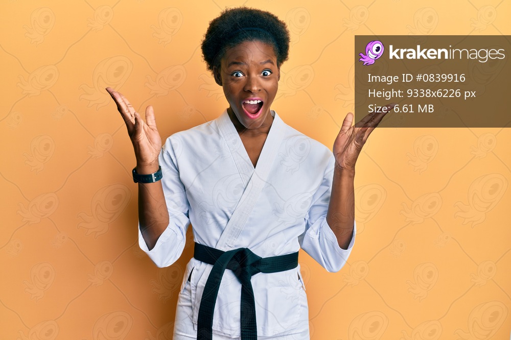 Young african american girl wearing karate kimono and black belt celebrating crazy and amazed for success with arms raised and open eyes screaming excited. winner concept 