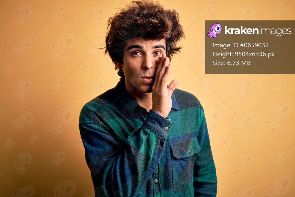 Young handsome man wearing casual shirt standing over isolated yellow background hand on mouth telling secret rumor, whispering malicious talk conversation