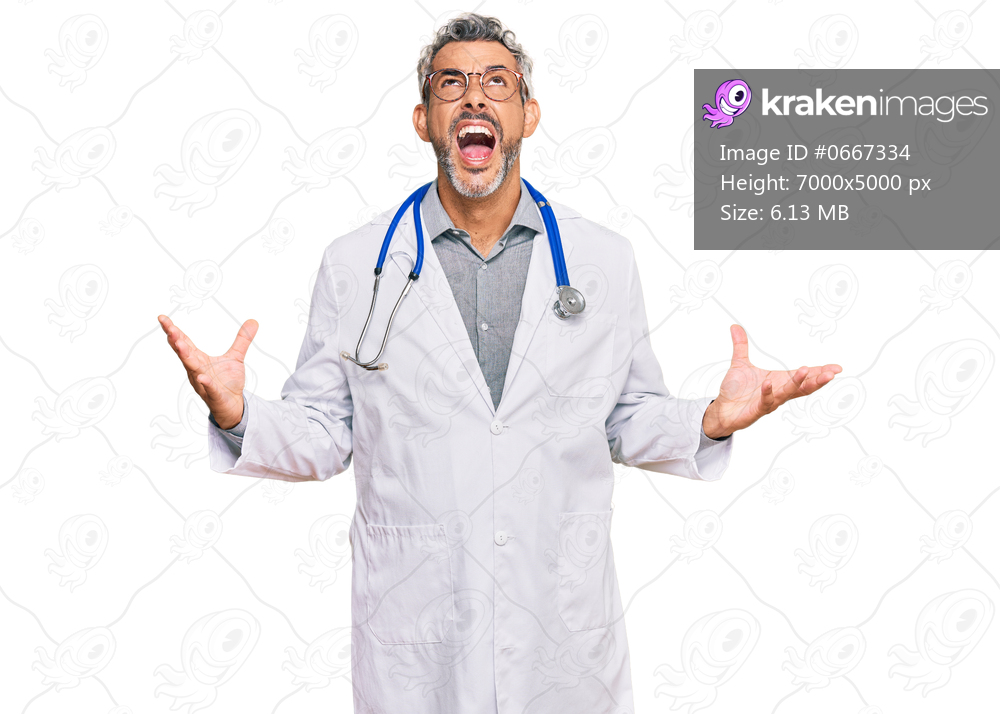 Middle age grey-haired man wearing doctor uniform and stethoscope crazy and mad shouting and yelling with aggressive expression and arms raised. frustration concept. 