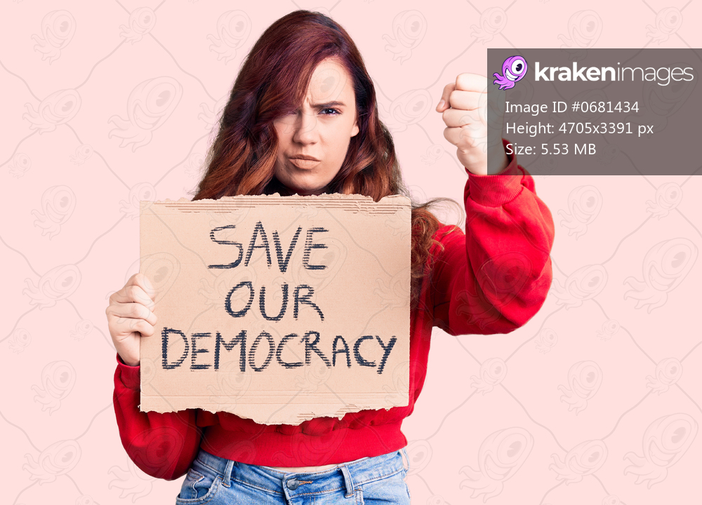 Young beautiful woman holding save our democracy protest banner annoyed and frustrated shouting with anger, yelling crazy with anger and hand raised 