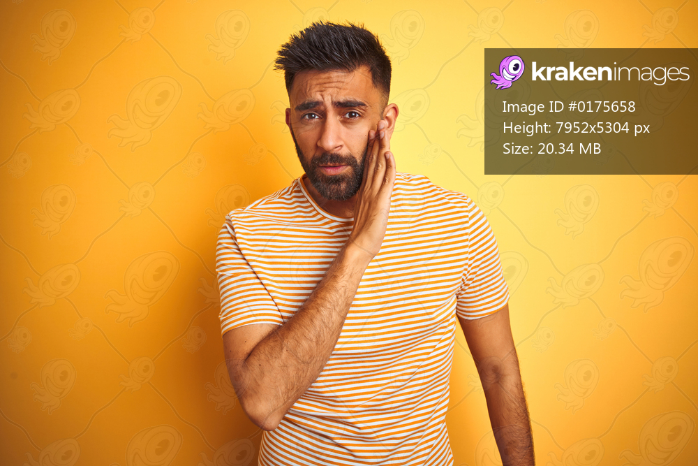 Young indian man wearing t-shirt standing over isolated yellow background hand on mouth telling secret rumor, whispering malicious talk conversation