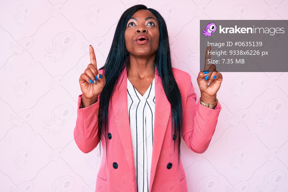 Young african american woman wearing business clothes amazed and surprised looking up and pointing with fingers and raised arms. 