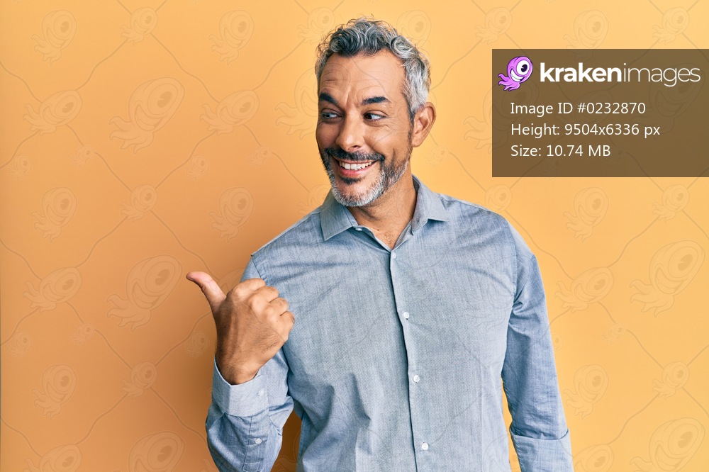 Middle age grey-haired man wearing casual clothes smiling with happy face looking and pointing to the side with thumb up. 