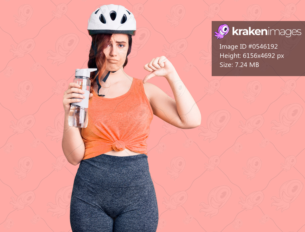 Young beautiful woman wearing bike helmet and holding water bottle with angry face, negative sign showing dislike with thumbs down, rejection concept 