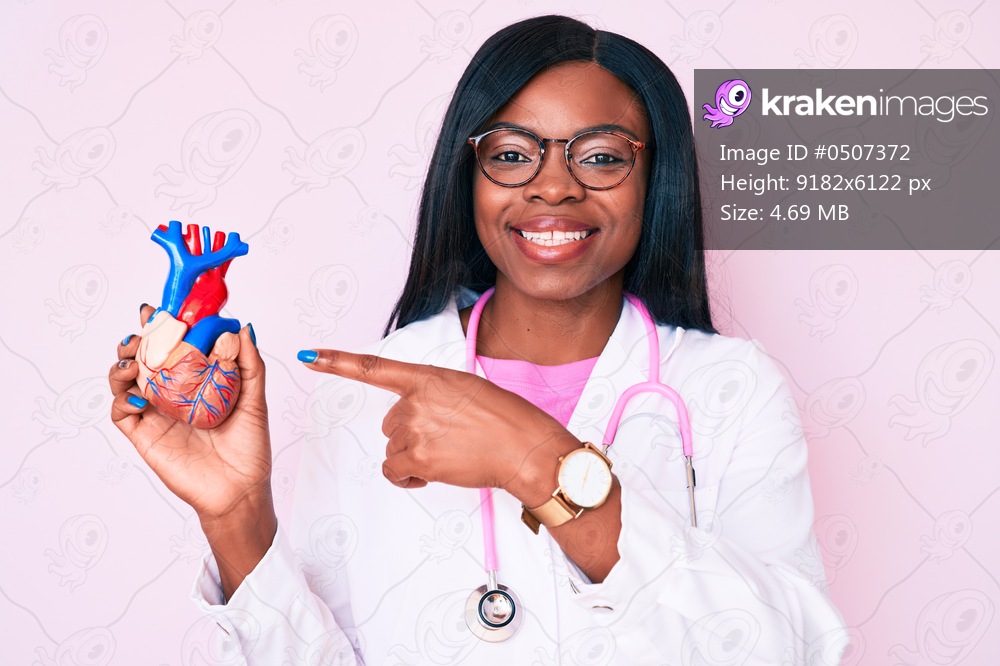 Young african american woman wearing doctor uniform holding heart smiling happy pointing with hand and finger 