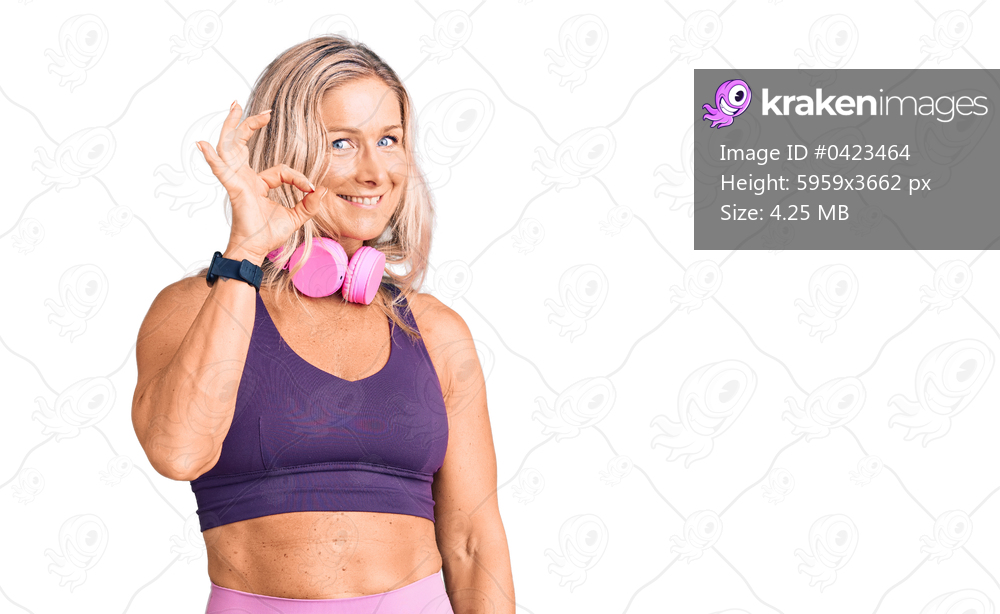 Middle age fit blonde woman wearing gym clothes and using headphones smiling positive doing ok sign with hand and fingers. successful expression. 
