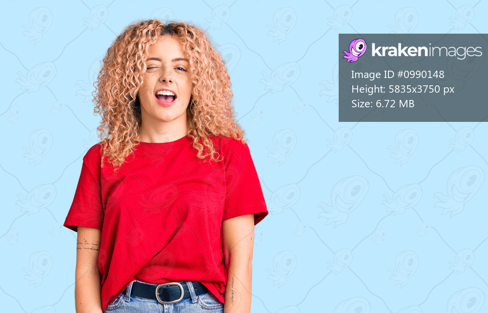Young blonde woman with curly hair wearing casual red tshirt winking looking at the camera with sexy expression, cheerful and happy face. 