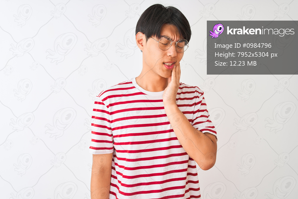 Young chinese man wearing glasses and striped t-shirt standing over isolated white background touching mouth with hand with painful expression because of toothache or dental illness on teeth. Dentist concept.