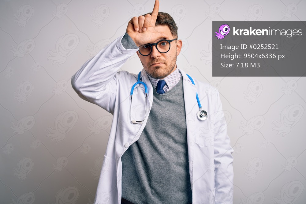 Young doctor man with blue eyes wearing medical coat and stethoscope over isolated background making fun of people with fingers on forehead doing loser gesture mocking and insulting.