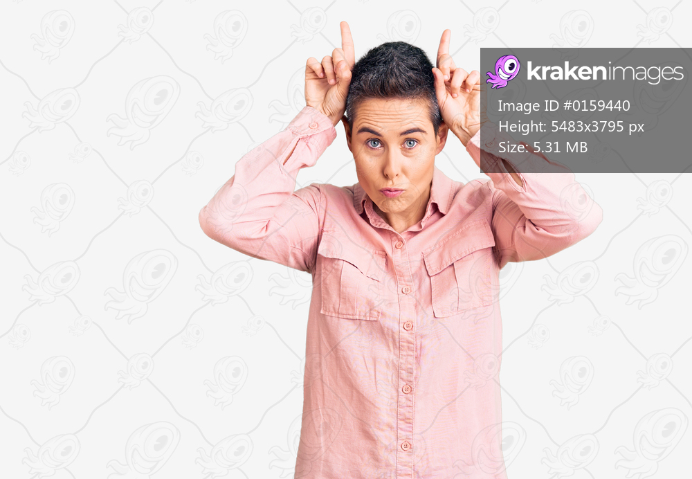 Young woman with short hair wearing casual clothes doing funny gesture with finger over head as bull horns 