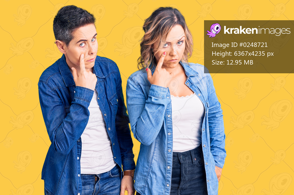Couple of women wearing casual clothes pointing to the eye watching you gesture, suspicious expression 