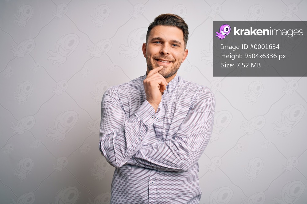 Young business man with blue eyes standing over isolated background looking confident at the camera with smile with crossed arms and hand raised on chin. Thinking positive.