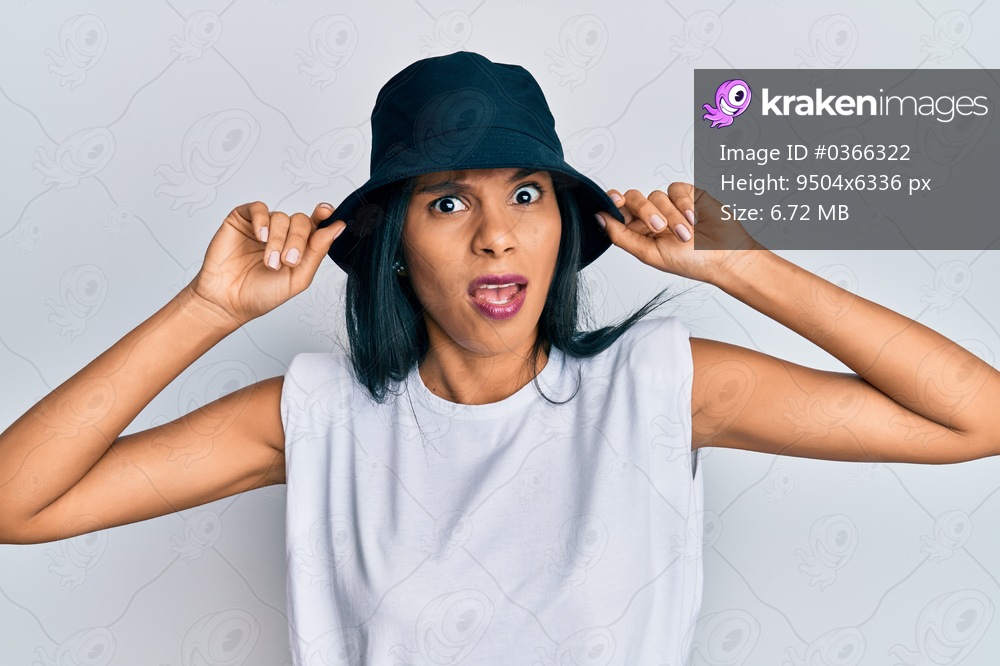 Young african american woman wearing fashion hat in shock face, looking skeptical and sarcastic, surprised with open mouth 