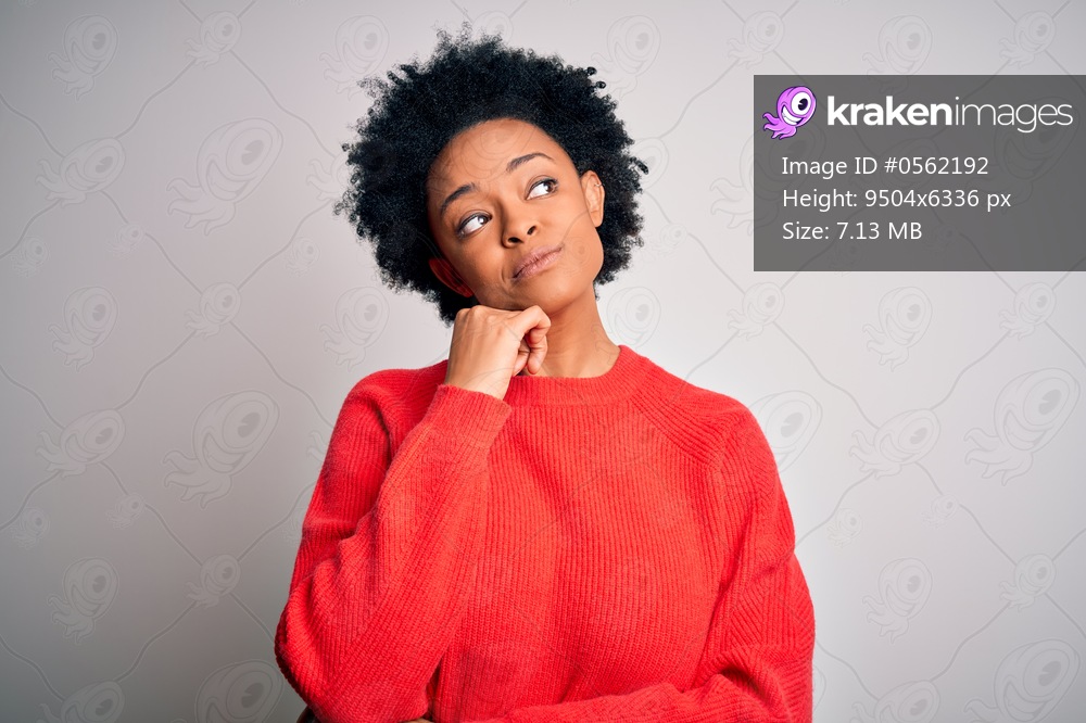 Young beautiful African American afro woman with curly hair wearing red casual sweater with hand on chin thinking about question, pensive expression. Smiling and thoughtful face. Doubt concept.