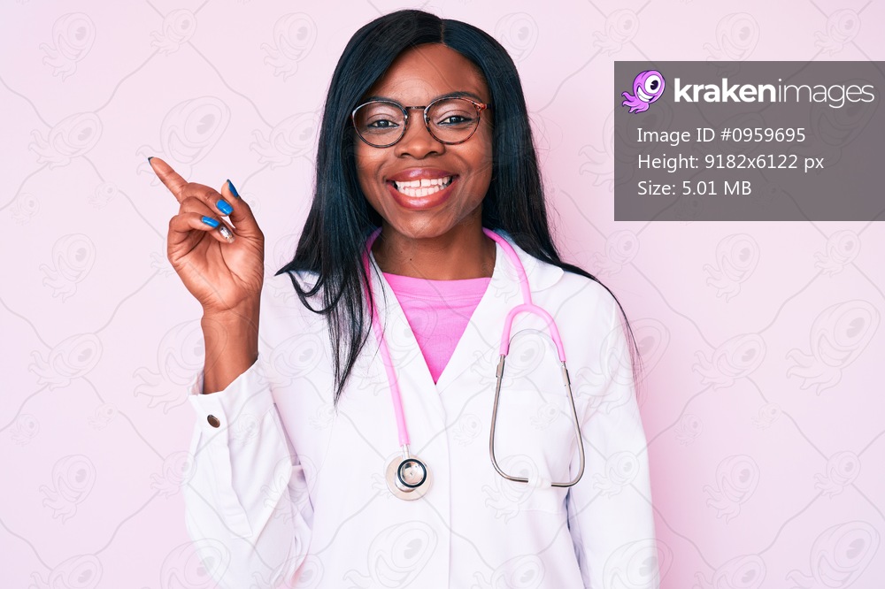 Young african american woman wearing doctor stethoscope smiling happy pointing with hand and finger to the side 