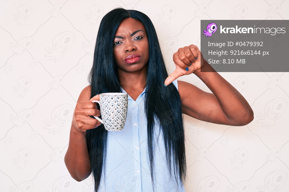Young african american woman holding coffee with angry face, negative sign showing dislike with thumbs down, rejection concept 