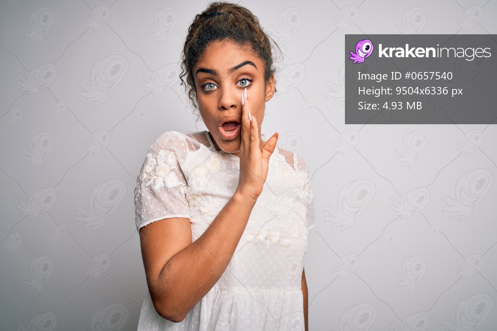 Young beautiful african american girl wearing casual t-shirt standing over white background hand on mouth telling secret rumor, whispering malicious talk conversation