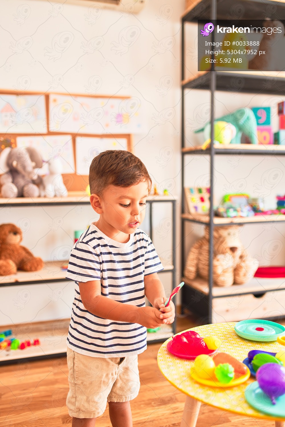 Beautiful toddler boy playing meals with plastic plates, fruits and vegetables at kindergarten