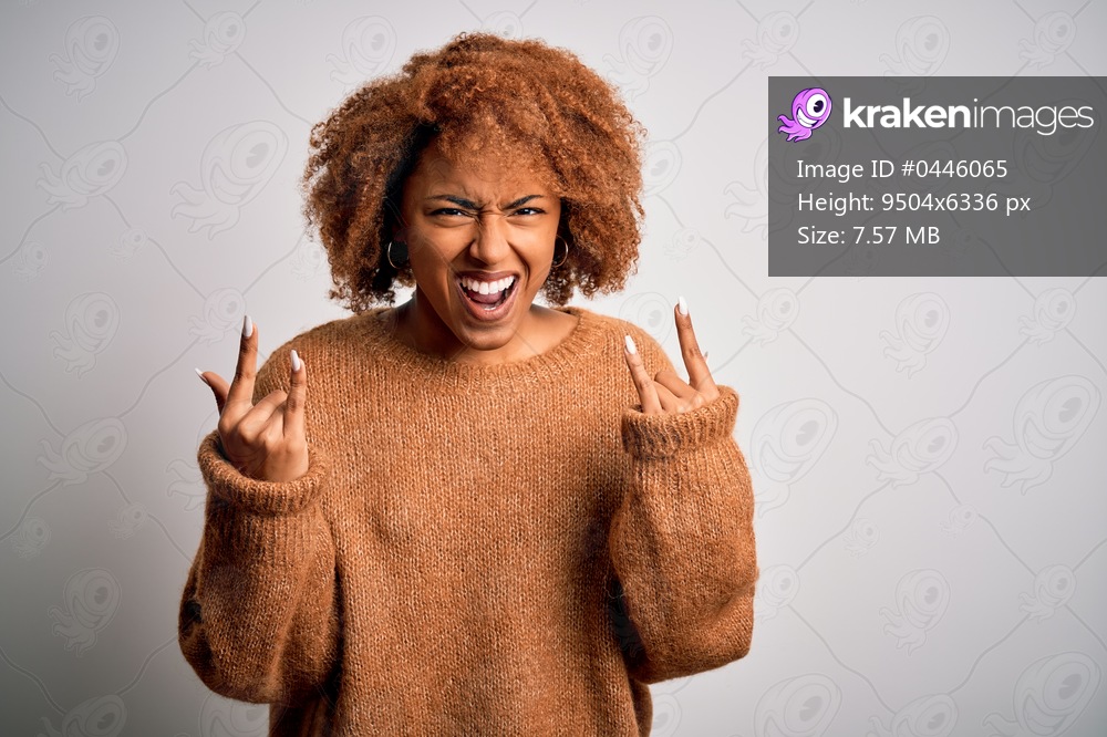 Young beautiful African American afro woman with curly hair wearing casual sweater shouting with crazy expression doing rock symbol with hands up. Music star. Heavy concept.