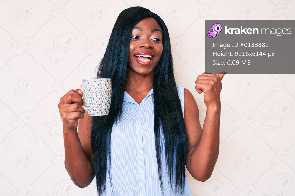 Young african american woman holding coffee pointing thumb up to the side smiling happy with open mouth 