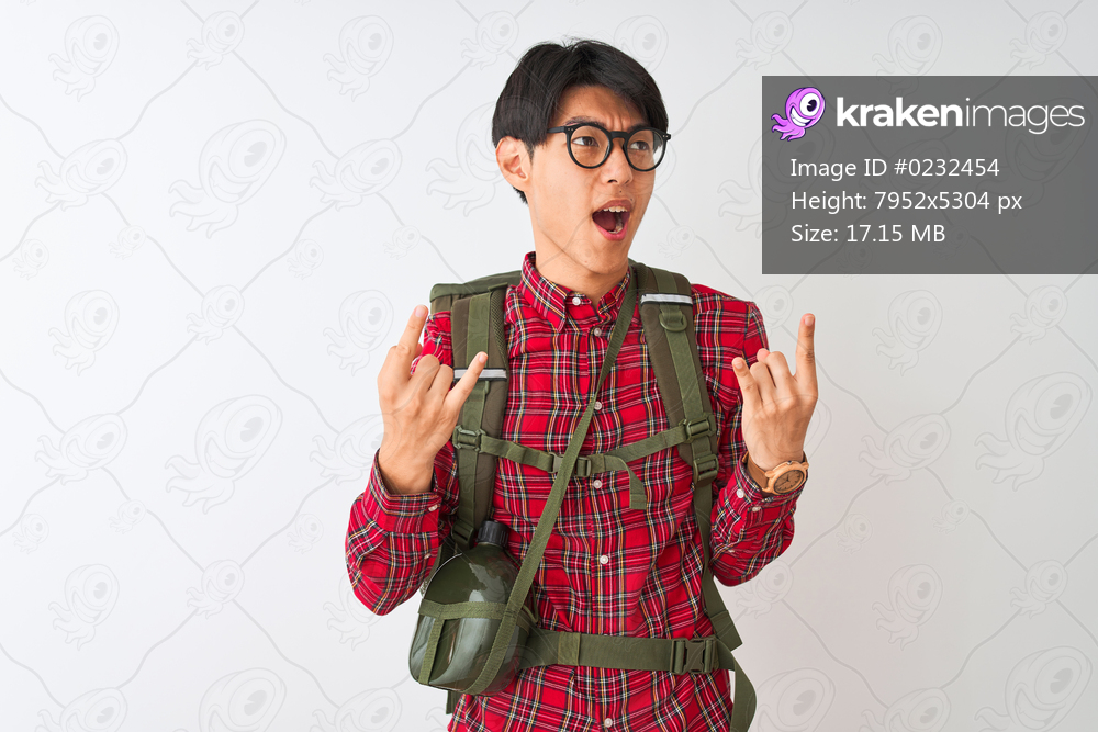 Chinese hiker man wearing backpack canteen glasses over isolated white background shouting with crazy expression doing rock symbol with hands up. Music star. Heavy concept.