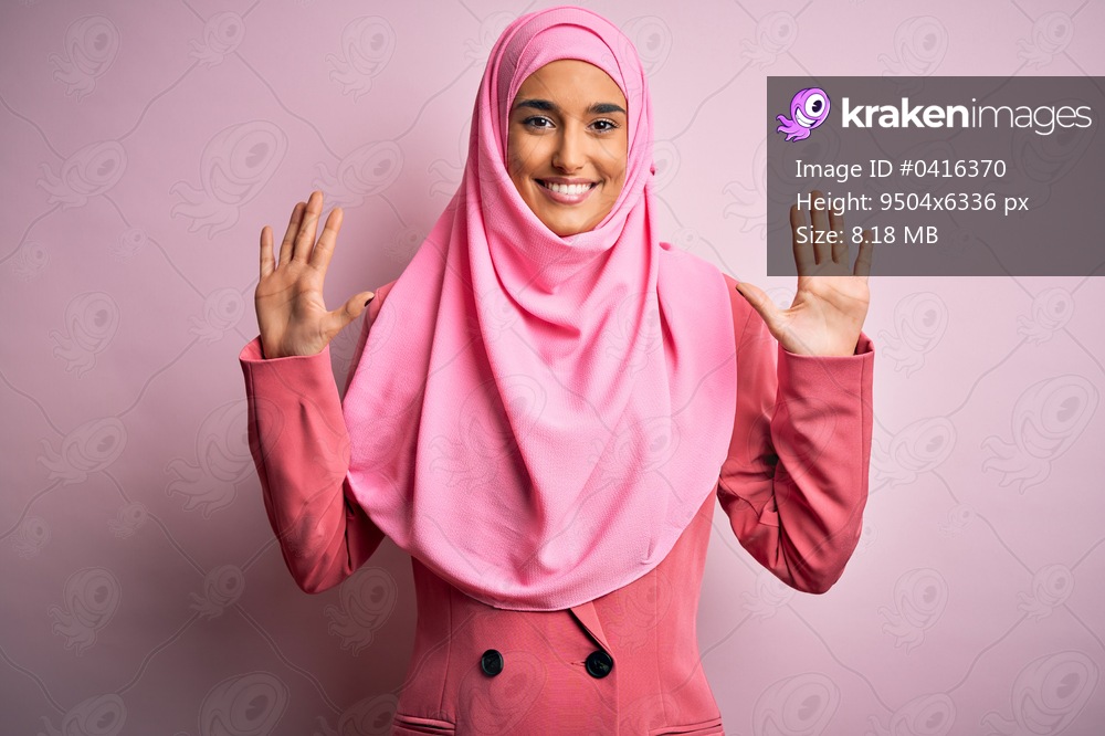 Young beautiful brunette businesswoman wearing pink muslim hijab and business jacket showing and pointing up with fingers number ten while smiling confident and happy.