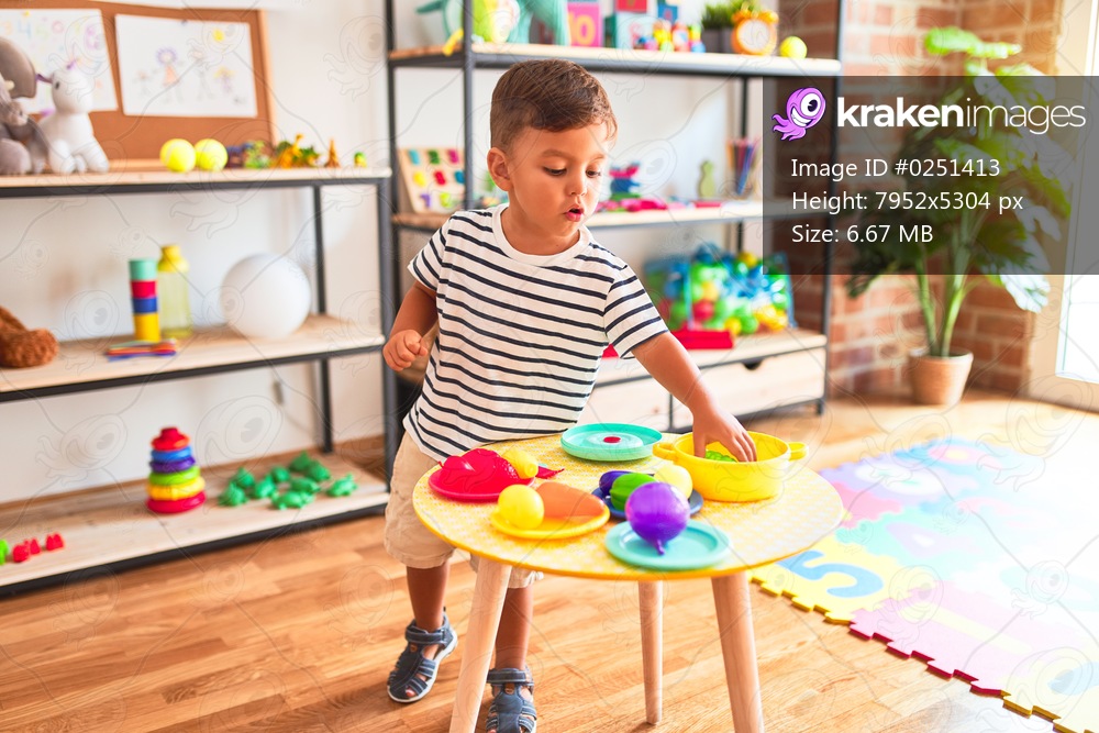 Beautiful toddler boy playing meals with plastic plates, fruits and vegetables at kindergarten