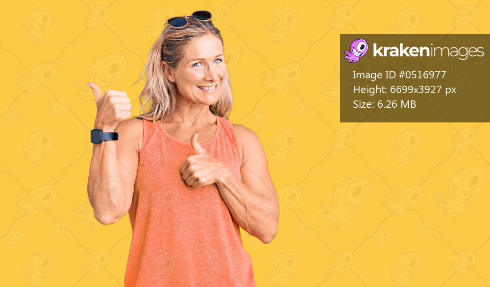 Middle age fit blonde woman wearing casual summer clothes and sunglasses pointing to the back behind with hand and thumbs up, smiling confident 