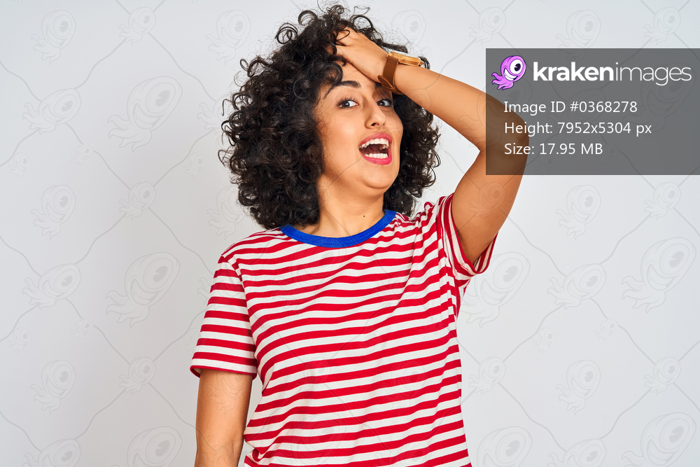 Young arab woman with curly hair wearing striped t-shirt over isolated white background surprised with hand on head for mistake, remember error. Forgot, bad memory concept.