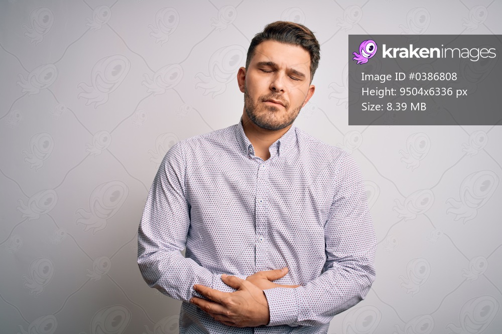Young business man with blue eyes standing over isolated background with hand on stomach because indigestion, painful illness feeling unwell. Ache concept.