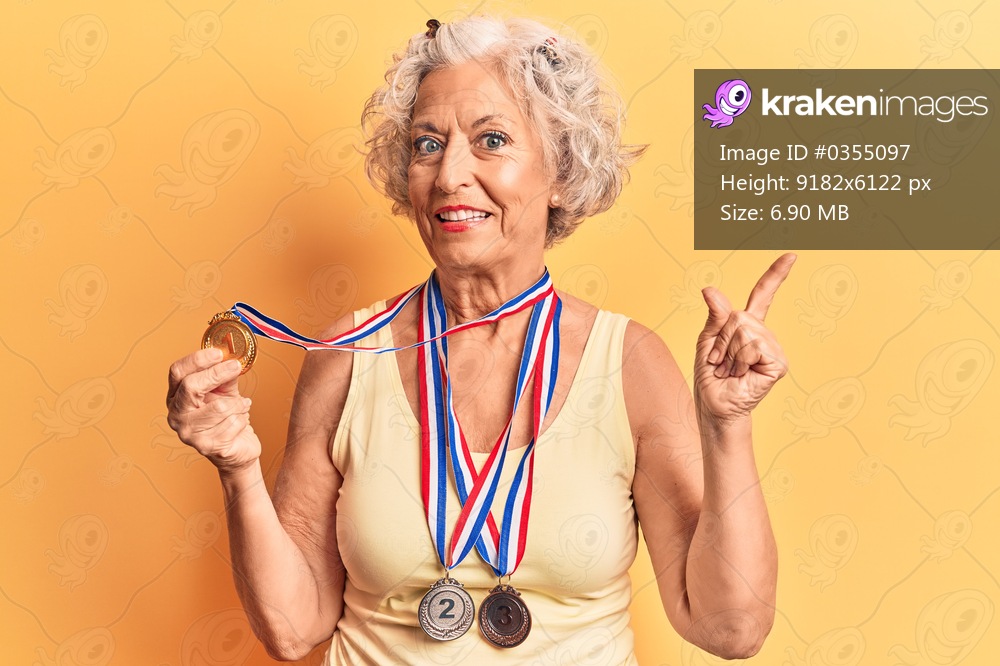 Senior grey-haired woman wearing medals smiling happy pointing with hand and finger to the side 