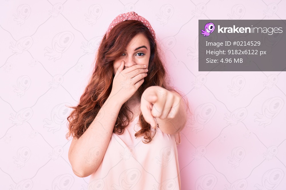 Young beautiful woman wearing casual clothes laughing at you, pointing finger to the camera with hand over mouth, shame expression 