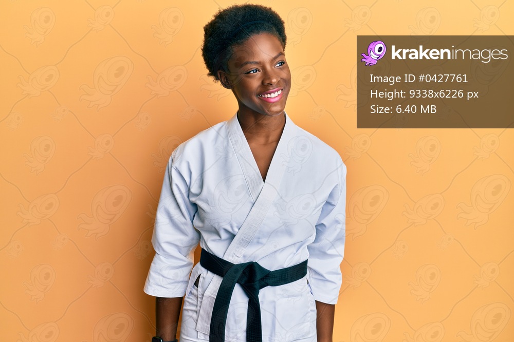 Young african american girl wearing karate kimono and black belt looking away to side with smile on face, natural expression. laughing confident. 