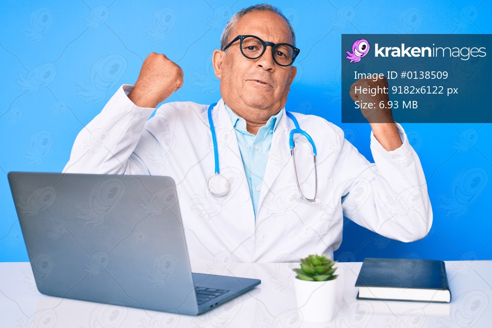 Senior handsome man with gray hair wearing doctor uniform working using computer laptop showing arms muscles smiling proud. fitness concept. 