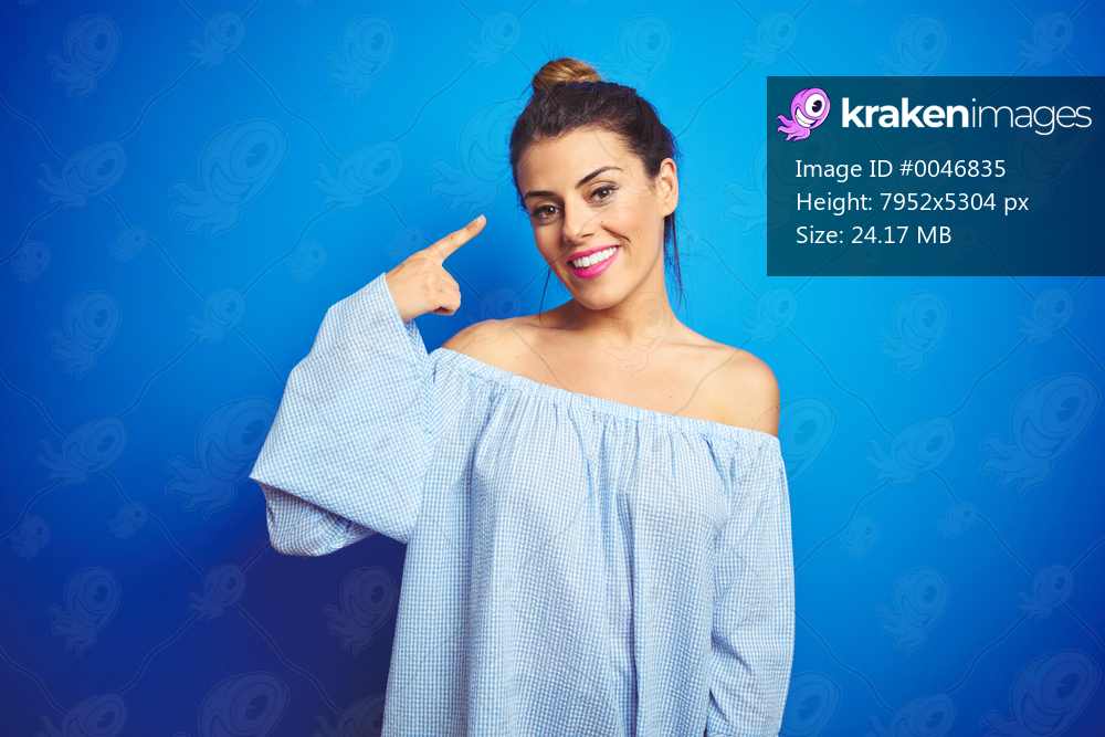 Young beautiful woman wearing bun hairstyle over blue isolated background Smiling pointing to head with one finger, great idea or thought, good memory