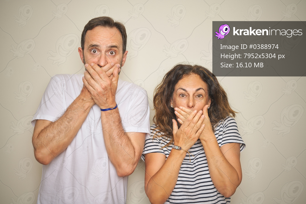 Beautiful middle age couple together standing over isolated white background shocked covering mouth with hands for mistake. Secret concept.