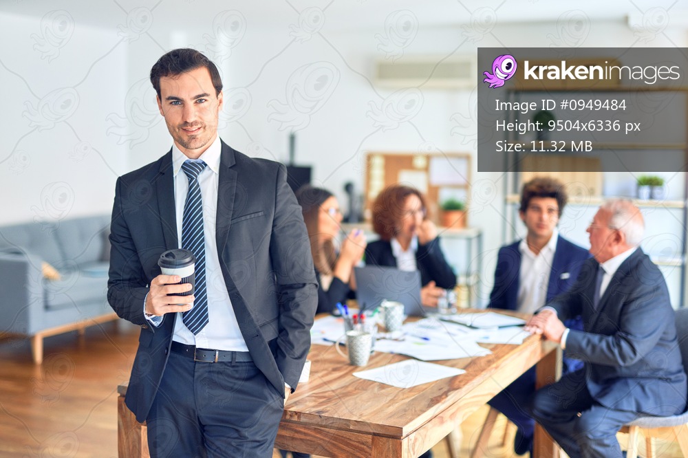 Group of business workers smiling happy and confident working together in a meeting. One of them, standing with smile on face looking at camera drinking coffee at the office.