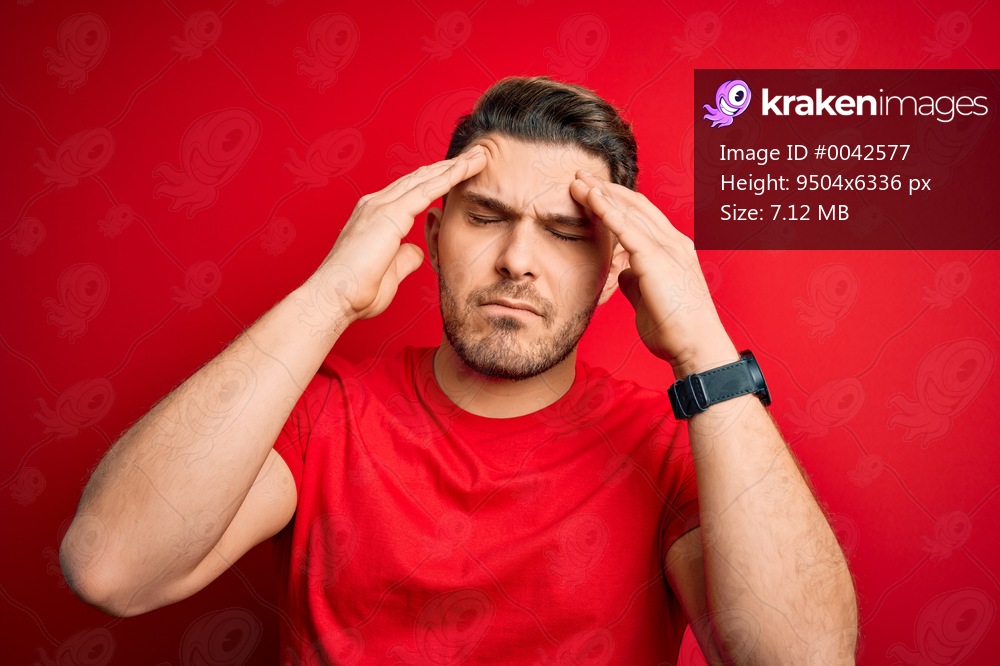 Young man with blue eyes wearing casual t-shirt over red isolated background suffering from headache desperate and stressed because pain and migraine. Hands on head.