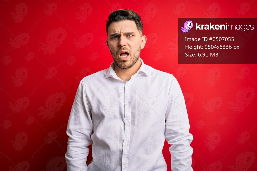 Young business man with blue eyes wearing elegant shirt standing over red isolated background In shock face, looking skeptical and sarcastic, surprised with open mouth