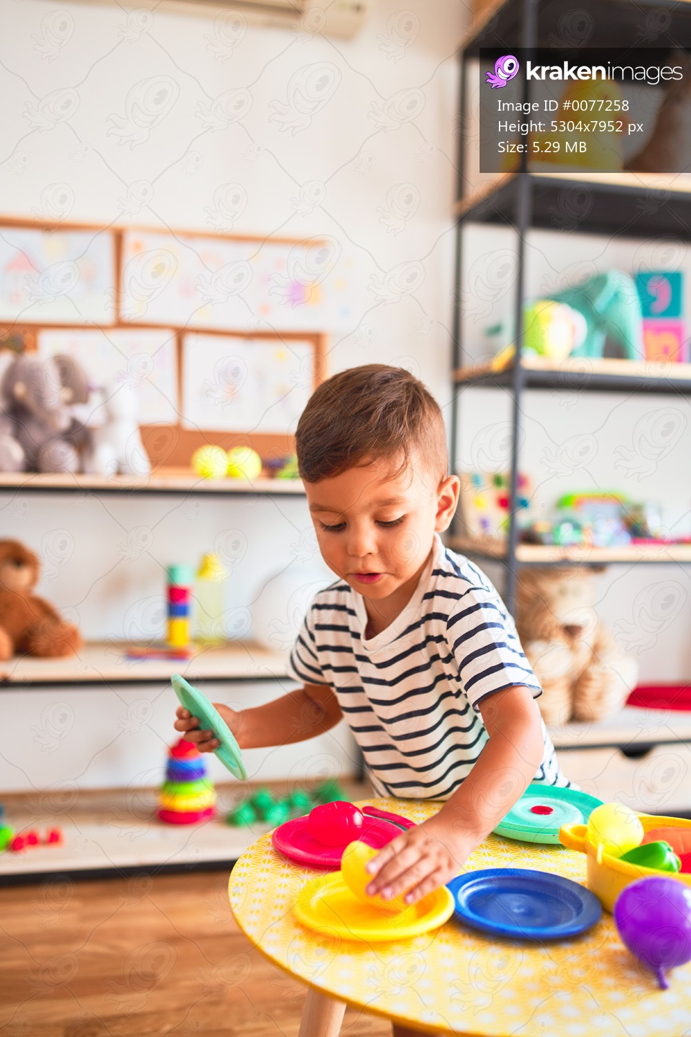 Beautiful toddler boy playing meals with plastic plates, fruits and vegetables at kindergarten