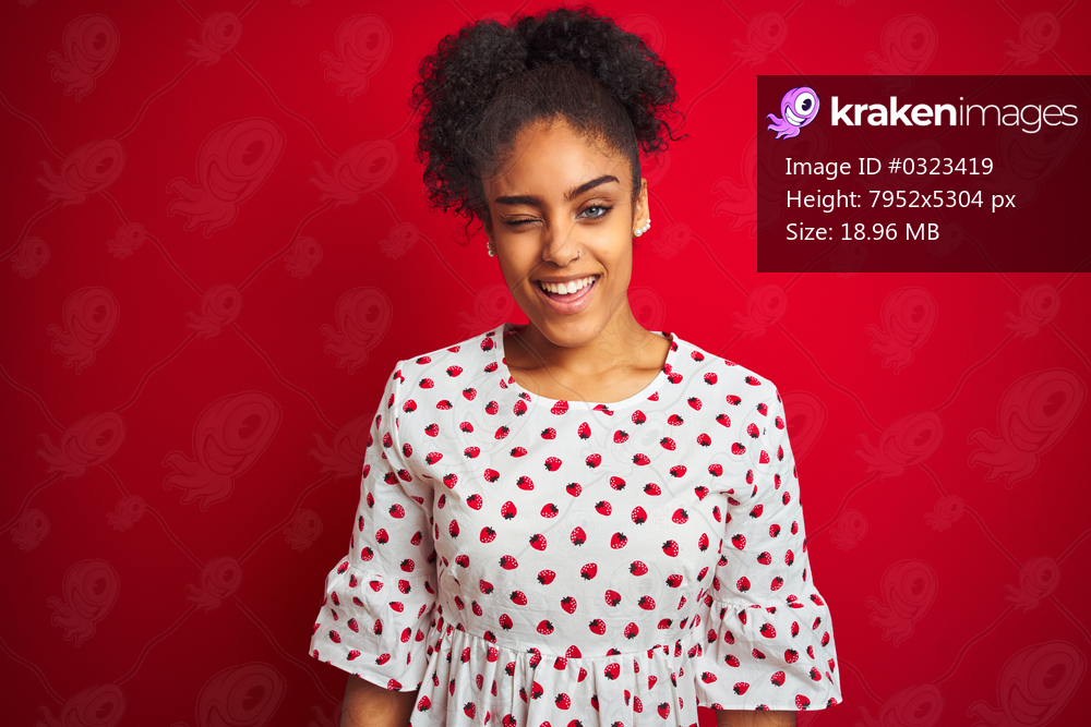 African american woman wearing fashion white dress standing over isolated red background winking looking at the camera with sexy expression, cheerful and happy face.