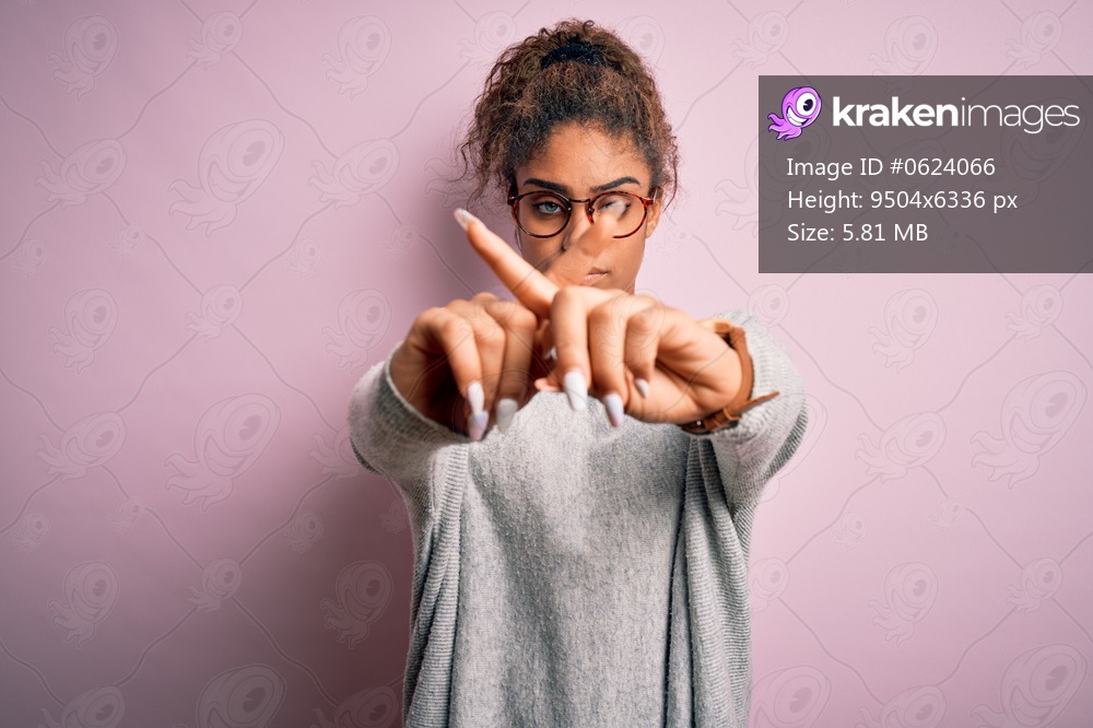 Young beautiful african american girl wearing sweater and glasses over pink background Rejection expression crossing fingers doing negative sign